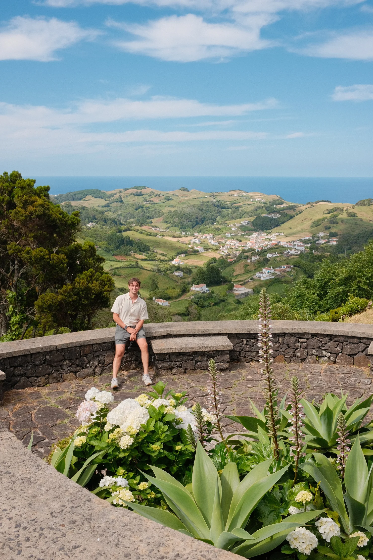 Liam Afonso standing on a green hillside above a village and the ocean in the Azores